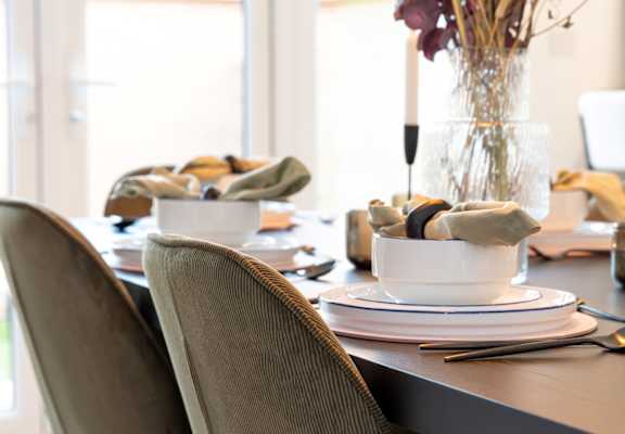 A table set for a meal with a vase of dried flowers in the center.