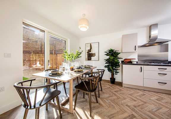 A dining room with a table set for two and a potted plant on the floor.