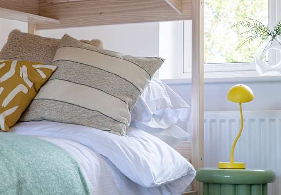 A bed with a green blanket and a yellow lamp.