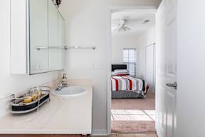 A bathroom with a sink, mirror, and bedroom in the background.
