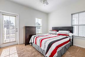 A bedroom with a bed, a dresser, and a window with blinds.