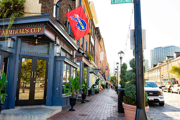 A street view of a city with a blue building on the left and a red flag hanging from a pole.
