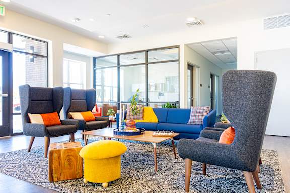 A living room with a grey sofa, a blue couch, and a yellow ottoman.