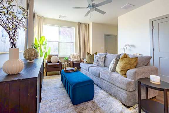 A living room with a grey couch, a blue ottoman, and a wooden side table.