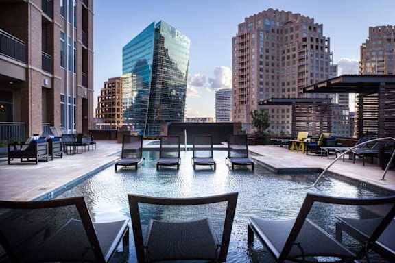 A pool with chairs around it in the foreground with buildings in the background. at Uptown by Onni Apartments, Apartments, Dallas, TX