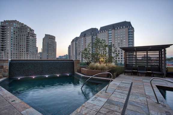 A pool area with a hot tub and a chair in front of a building. at Uptown by Onni Apartments, Apartments, Dallas, TX