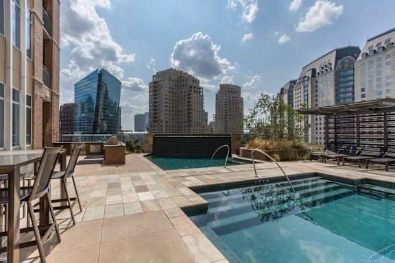 A swimming pool with a chair and a table is in the foreground with buildings in the background. at Uptown by Onni Apartments, Apartments, Dallas, TX