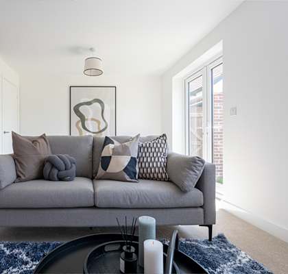 A grey couch with pillows and a candle on a table.