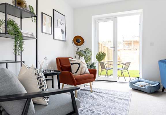 A living room with a grey couch, a red chair, a table with a vase and a plant on it, and a blue pet bed.