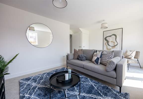A living room with a grey couch and a round mirror on the wall.