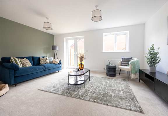 A blue couch sits in a living room with a grey rug and a small table with a vase on it.
