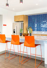 A kitchen with a white counter top and orange chairs.