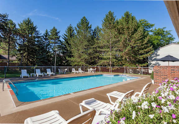 A pool surrounded by trees and chairs.