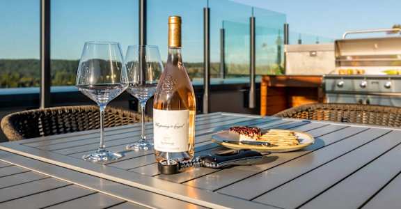 A bottle of wine is on a table with two glasses and a plate of food.
