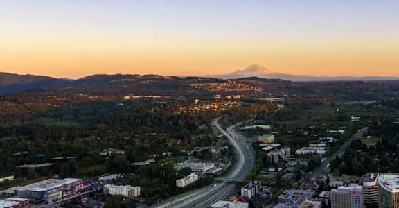 A cityscape with a mountain in the background and a crescent moon in the sky.