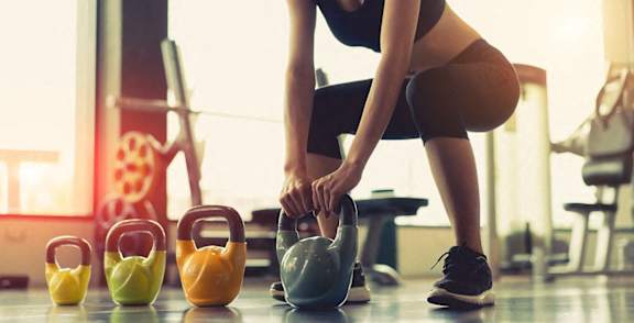 A woman is squatting and lifting a kettlebell in a gym.