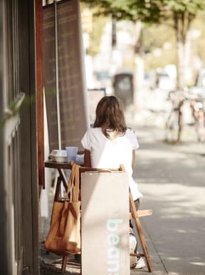 a woman sitting at a table outside of a coffee shop on the sidewalk