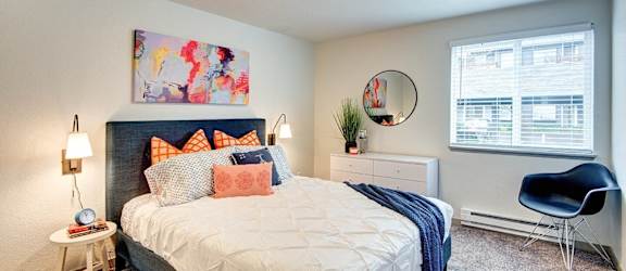 A bedroom with a bed, chair, and a painting on the wall.