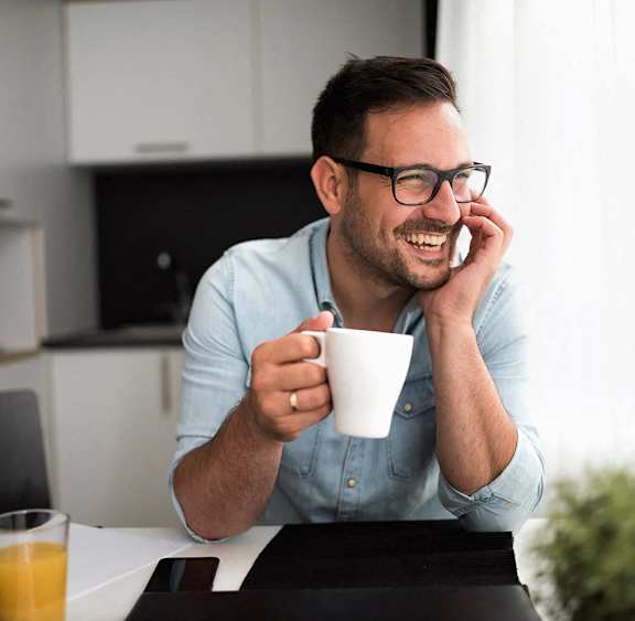 A man in glasses is smiling while holding a white cup.
