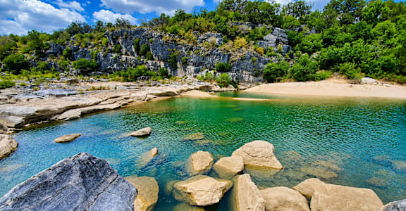 A beautiful beach with rocks in the foreground and a cliff in the background.