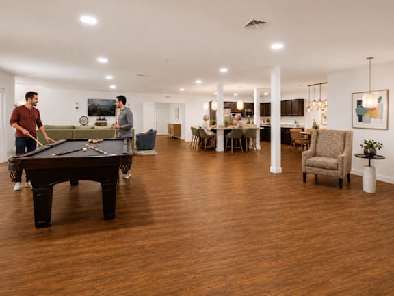 Two men playing pool in a room with a pool table.