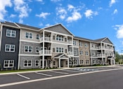 Thumbnail 1 of 10 - A large apartment complex with a parking lot in front.