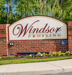 A sign for Windsor Crossing with a brick wall and flowers.