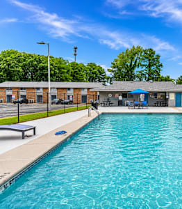 A large outdoor swimming pool with a blue sky and trees in the background.