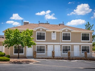 A beige two-story house with a white fence and a tree in front.