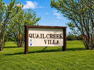 A sign that says Quail Creek Villa stands in a grassy field.