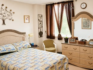 A bedroom with a bed, chair, and a clock on the wall.