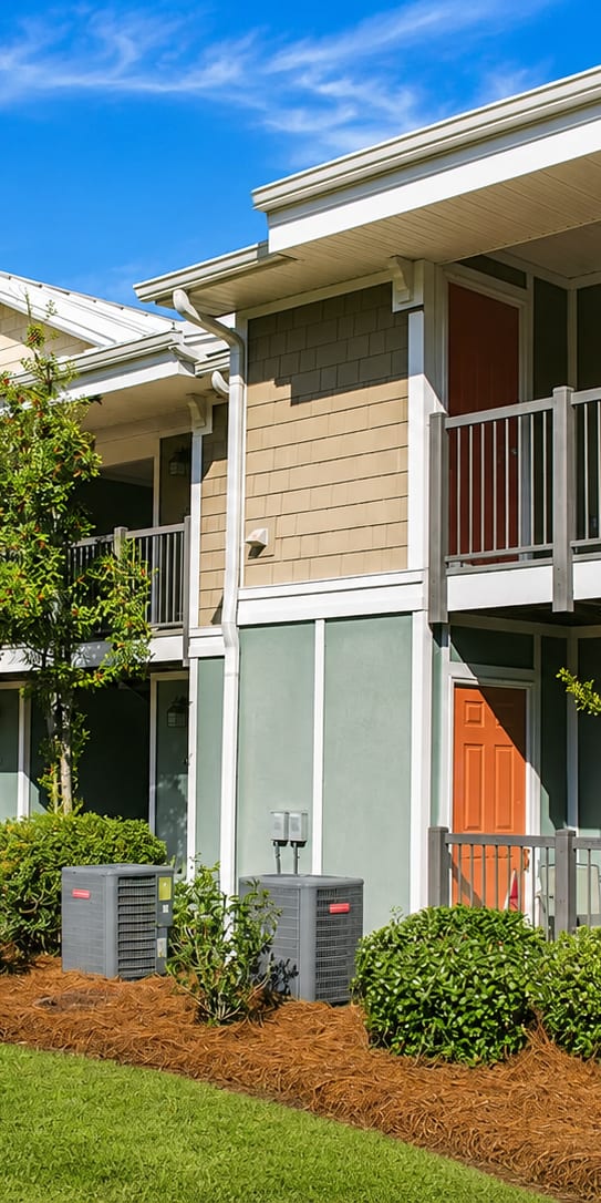 A row of townhouses with green lawns and bushes in front.