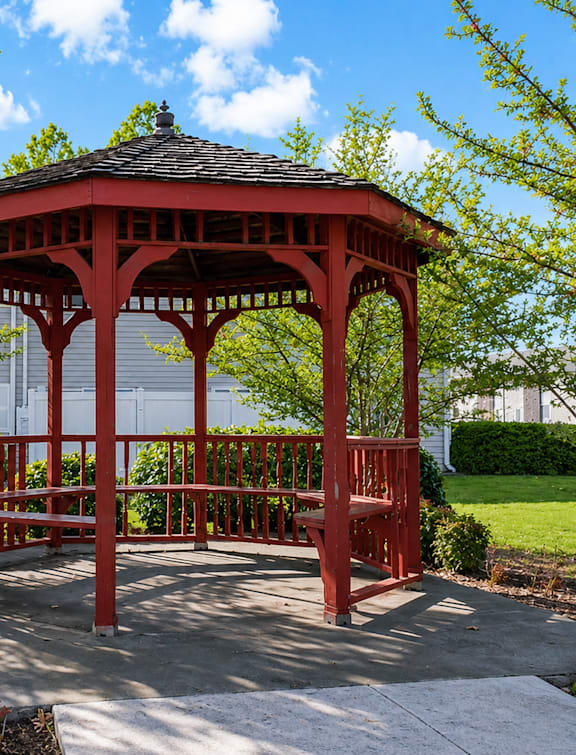 A red gazebo is surrounded by trees and bushes.