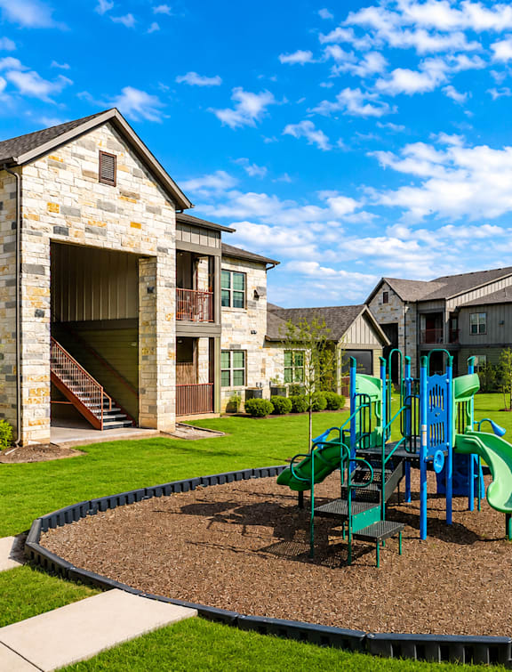 A playground with a green slide and a blue swing set in the middle of a gravel area.
