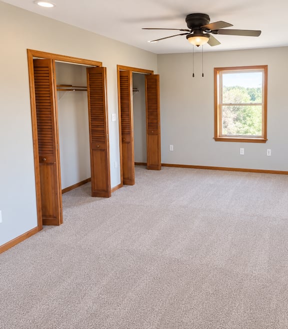 A room with a ceiling fan and two windows.