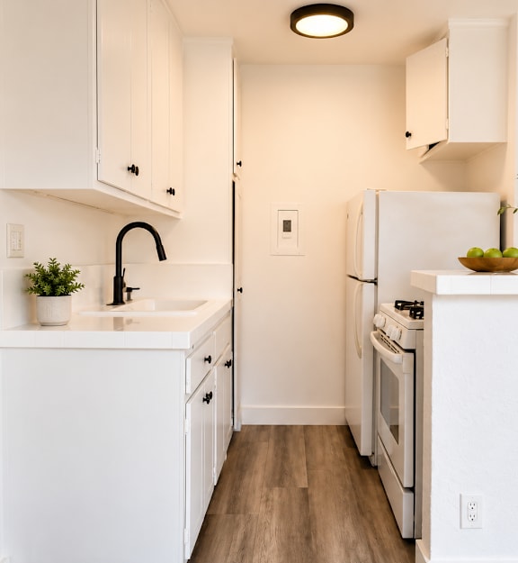 A white kitchen with a sink, stove, and refrigerator.