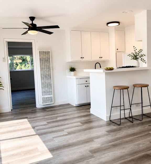 A kitchen with white cabinets and a white island with two stools.