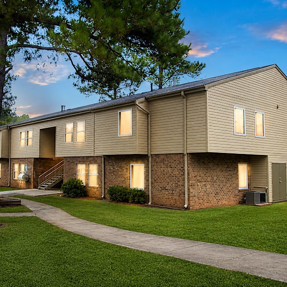 A building with a brown siding and a brick wall is surrounded by a grassy area and trees.