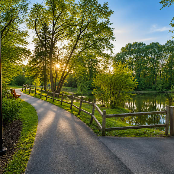 a path next to a pond with trees and a fence
