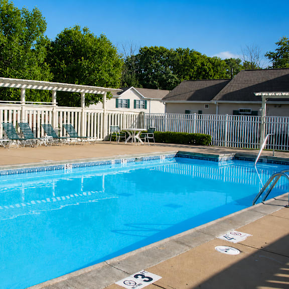 A blue swimming pool with a white fence and trees in the background.