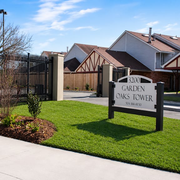 A sign for Garden Oaks Tower is in front of a black gate.