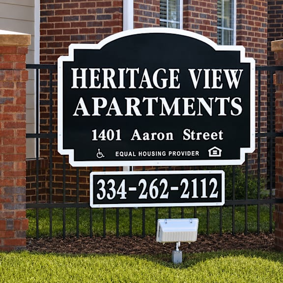A sign for Heritage View Apartments is displayed in front of a brick wall.