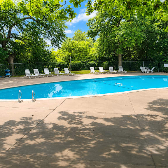A swimming pool surrounded by trees and chairs.