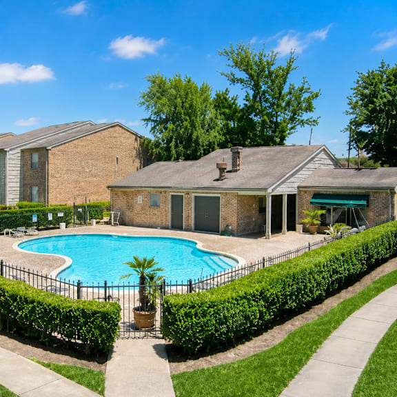A pool surrounded by a black fence and green bushes.