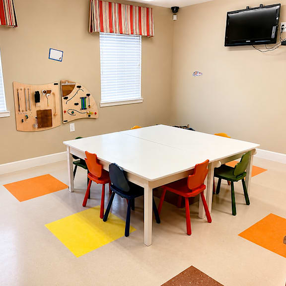 A white table surrounded by colorful chairs in a room with a television on the wall.
