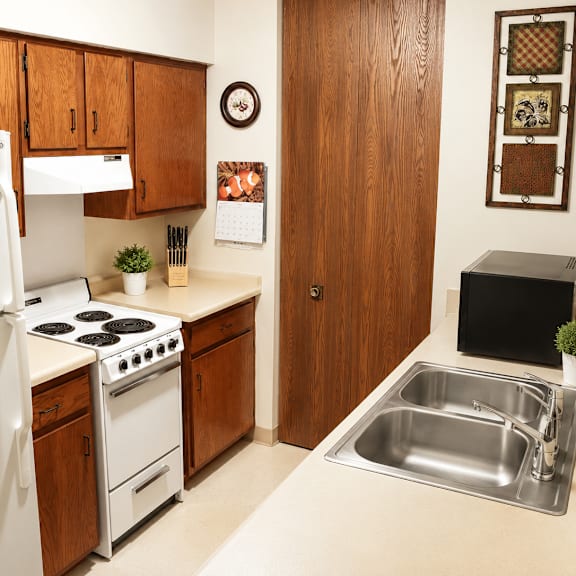 A kitchen with a white refrigerator, wooden cabinets, a stove, and a sink.