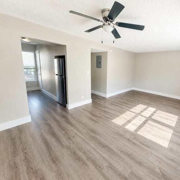 A spacious room with a ceiling fan and a refrigerator.