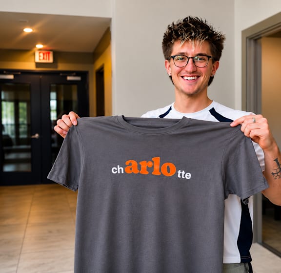 A man holding a grey shirt with the word "charlotte" written on it.