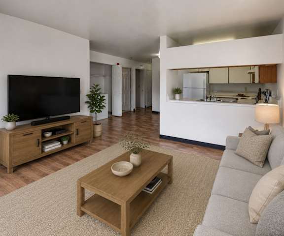 A view of the large empty living room with windows, a fireplace, and a door the balcony and the kitchen with white appliances and white wooden large cabinets at Silver Ridge Apartment Homes. 