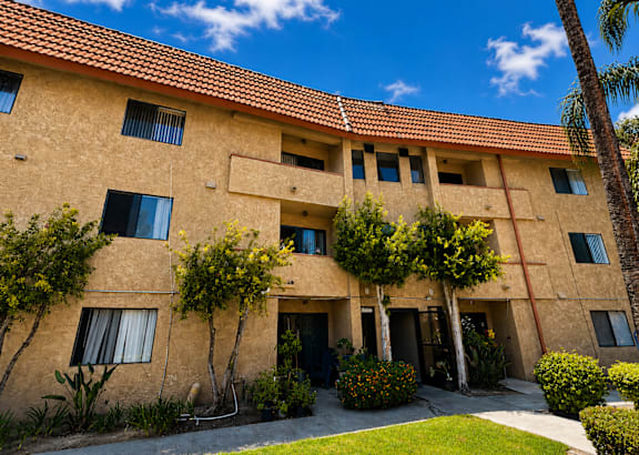 A building with a red roof and beige walls with windows and plants in front.